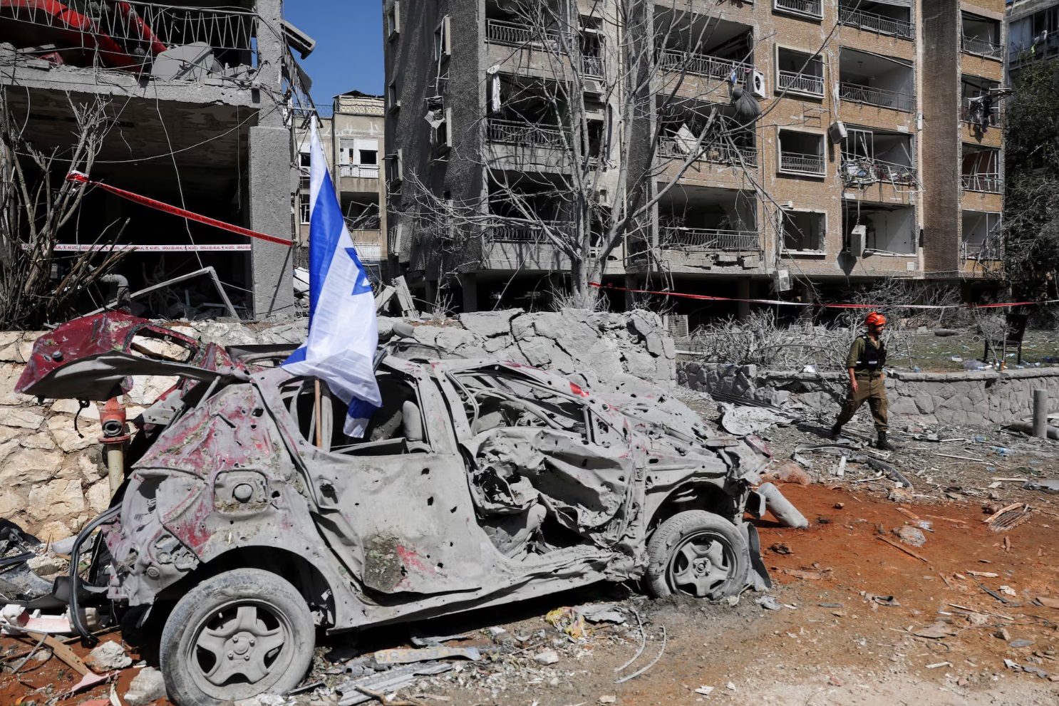 在以色列拉马特甘，一名救援人员走过伊朗导弹袭击现场一辆受损车辆旁